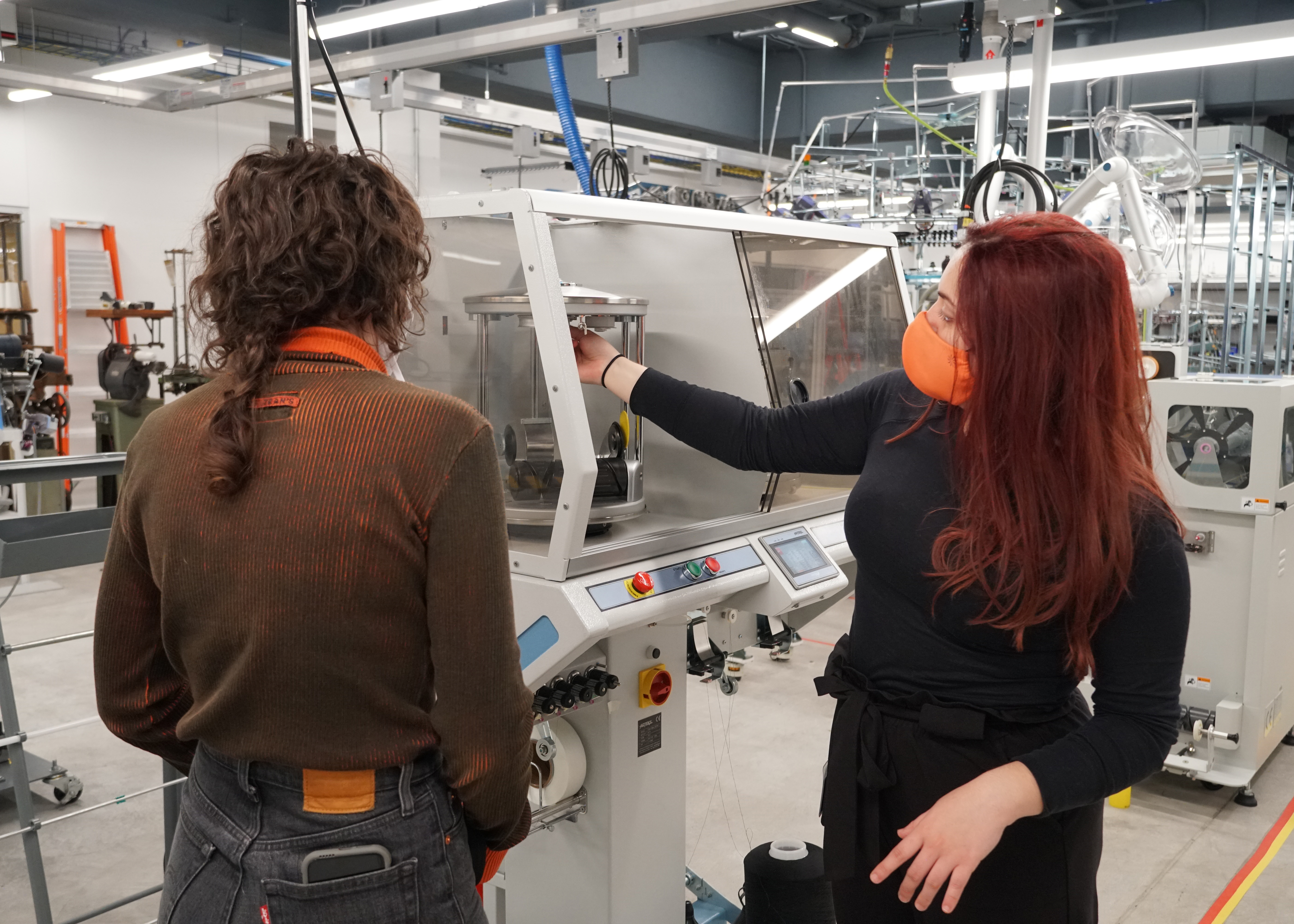 Two people in a large manufacturing space stand near a machine